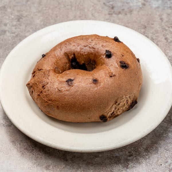 A chocolate chip bagel from Pizagel's Pizza & Bakery, on a white plate.