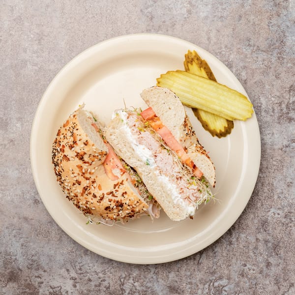 Everything bagel sandwich with cream cheese, sprouts, and tomato, served with pickle slices.