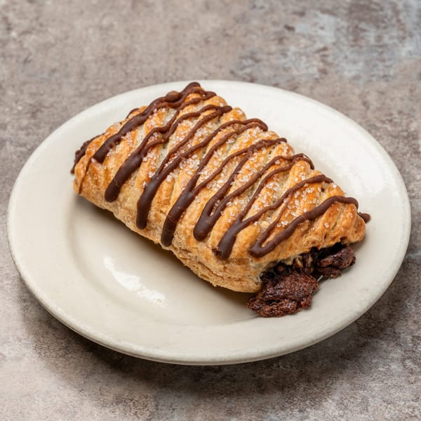 Pizagel's chocolate-filled pastry with chocolate drizzle and sugar crystals on a white plate.