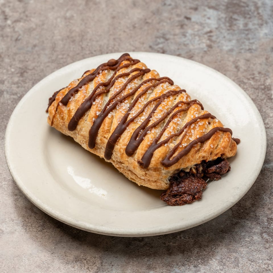 Pizagel's chocolate-filled pastry with chocolate drizzle and sugar crystals on a white plate.