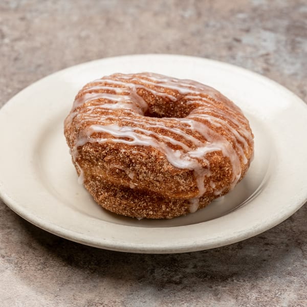 A Pizagel's cinnamon sugar donut with white icing drizzle on a white plate.