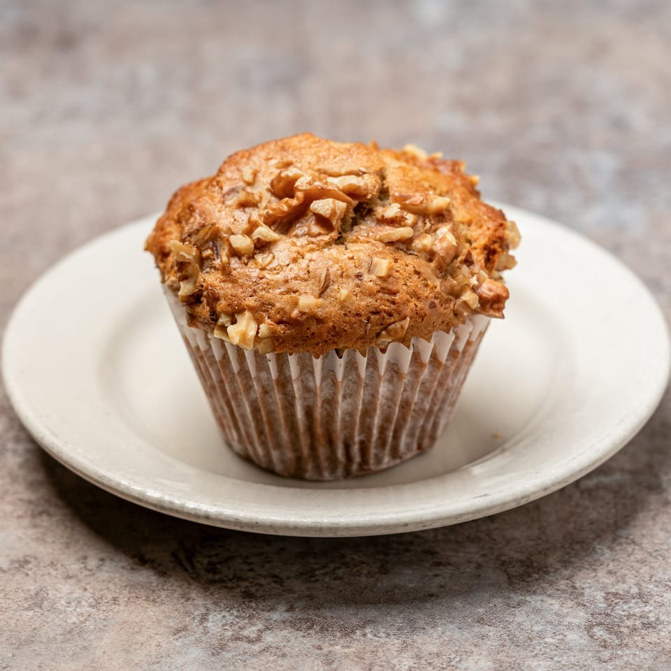 A Pizagel's Bakery muffin with walnuts on a white plate.