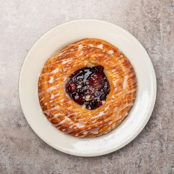 A Pizagel's danish pastry with fruit filling and white icing drizzle on a white plate.