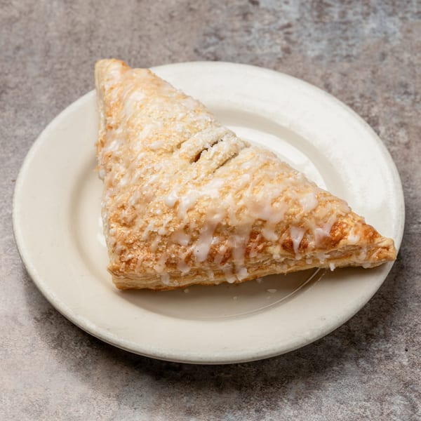 A triangular pastry with white icing and sugar crystals on a white plate from Pizagel's Bakery.