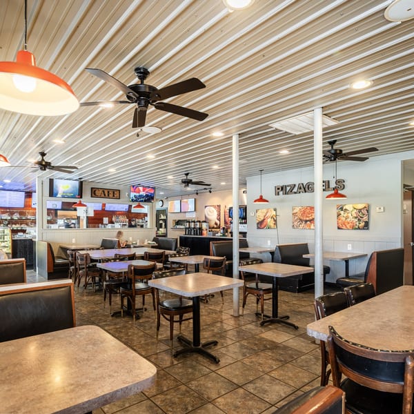 Spacious Pizagel's Pizza & Bakery dining room with tables, booths, ceiling fans, and pizza art.